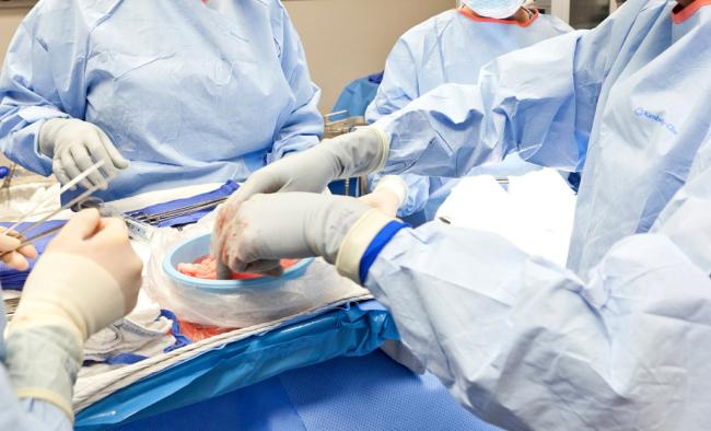Four surgeons in blue gowns around an operating table.