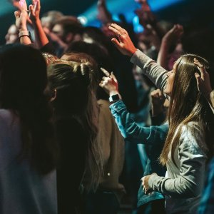 Young people raise their arms in worship at a group service.