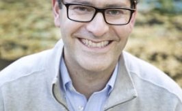Headshot of a white man with short brown hair and glasses wearing a tan half zip with the Ralph Lauren Polo Logo