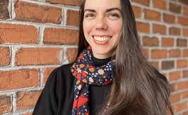 Woman with long dark hair standing in front of a brick wall 