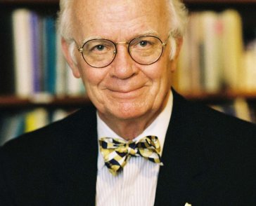 Bald man in glasses and bowtie in front of a book case