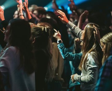 Young people raise their hands in worship in a group setting. 