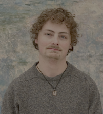 Headshot of a man with curly hair and a moustache