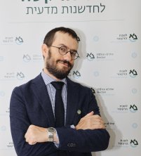 Headshot of a man in front of a Hebrew step and repeat