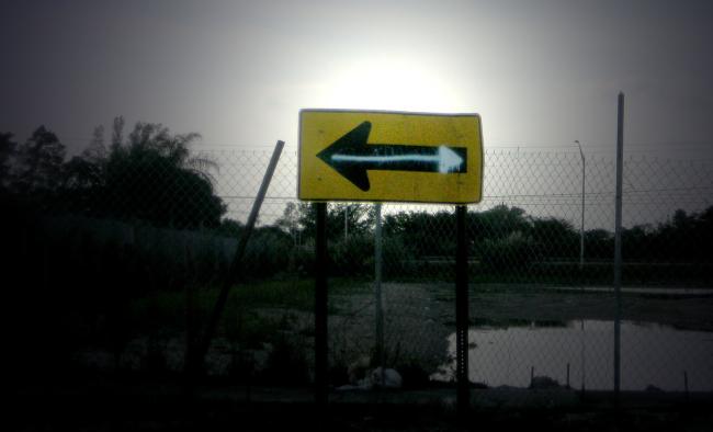 A road sign with an arrow pointing left has been altered with graffiti to point right
