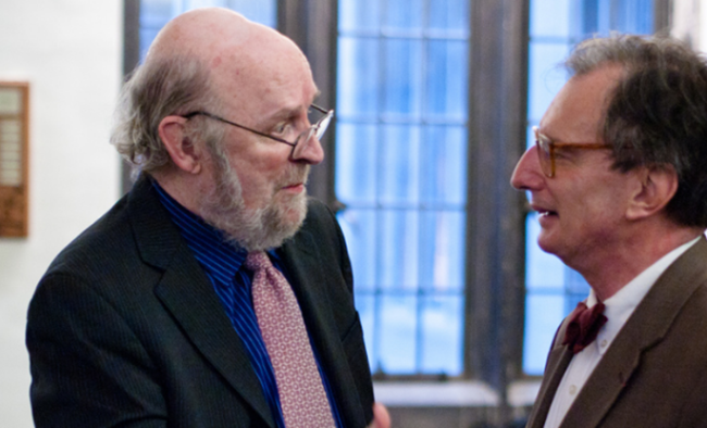 Two men in suit jackets and glasses facing each other