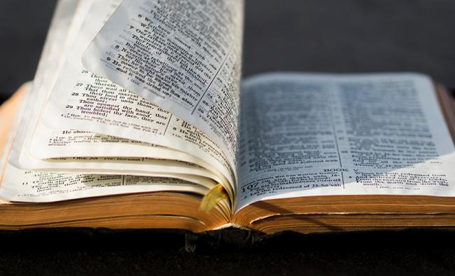 Bible lying flat on table with several pages upright as if being turned