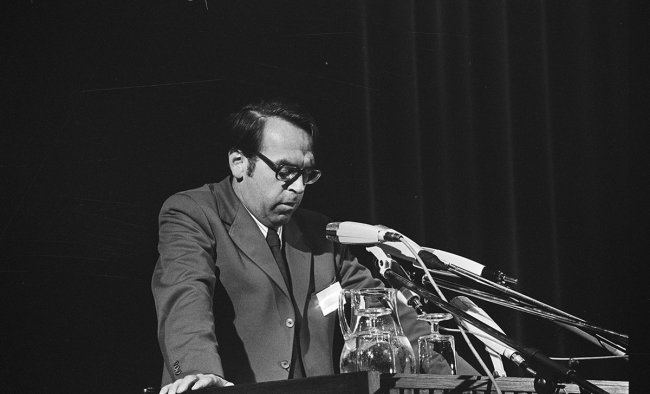 Jürgen Moltmann stands at a podium and speaks into several microphones