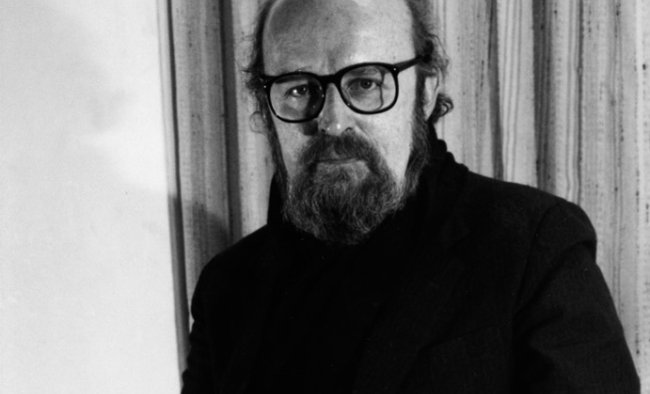 A black and white portrait of a bald man with a beard and glasses wearing a black cassock