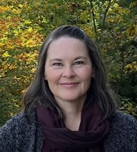 Headshot of a woman with long dark hair before trees
