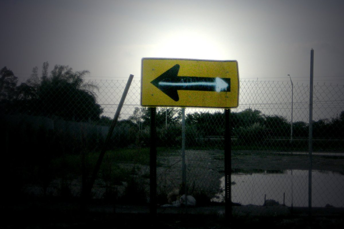 A road sign with an arrow pointing left has been altered with graffiti to point right