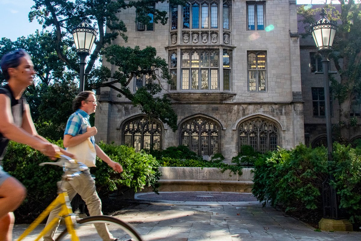 Woman on a bike and man with yellow bag walk by the exterior of Swift Hall