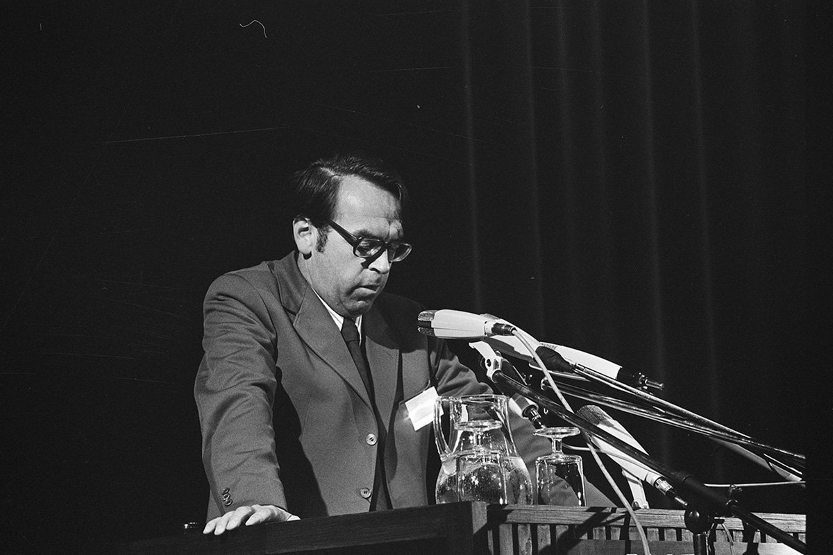 Jürgen Moltmann stands at a podium and speaks into several microphones