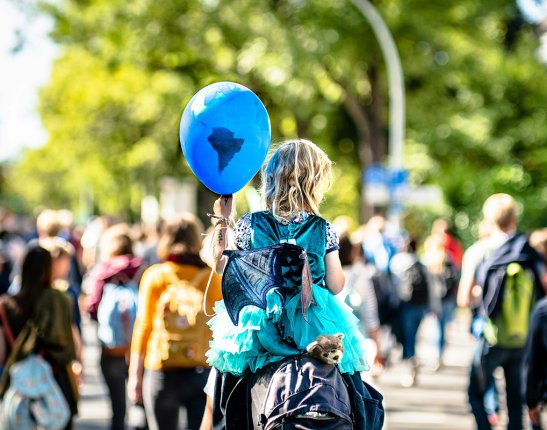 A man carries a child holding a blue balloon decorated as the earth 