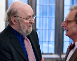 Two men in suit jackets and glasses facing each other