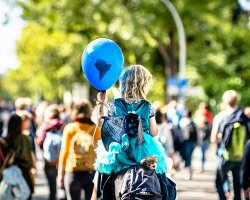 A man carries a child holding a blue balloon decorated as the earth 