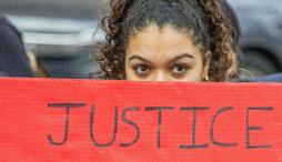 Woman peering out from behind red sign stating JUSTICE