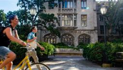 Woman on a bike and man with yellow bag walk by the exterior of Swift Hall