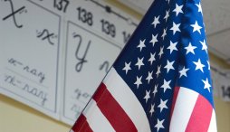 An American flag hangs in a classroom with the English alphabet on the wall behind it.